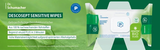 Werbegrafik für Dr. Schumacher DESCOSEPT SENSITIVE WIPES – gebrauchsfertige Desinfektionstücher. Grüner Hintergrund mit Blättern als Natur-Symbolik. Links Textkästen mit Produktvorteilen: „Aus 100 % nachwachsenden Rohstoffen“, „Begrenzt viruzid PLUS in 3 Minuten“ und „Hohe Materialverträglichkeit aufgrund optimierten Alkoholgehalts“. Rechts eine Packung der Tücher mit Bio-Siegel „DESOTEX BIO VLIES“ und Symbolen für Hautfreundlichkeit und Nachhaltigkeit.