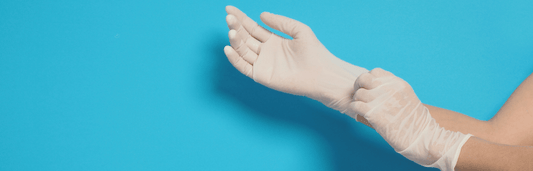 Person zieht einen weißen Einweghandschuh über die Hand, vor blauem Hintergrund in Nahaufnahme