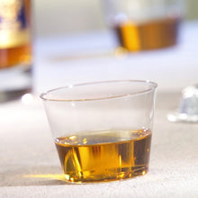 Ein Starpak 15 Trinkbecher, PS 0,1 l glasklar, enthält eine kleine Menge bernsteinfarbener Flüssigkeit auf einer hellen Oberfläche, während im Hintergrund ein weiterer Becher und eine Flasche unscharf sind.