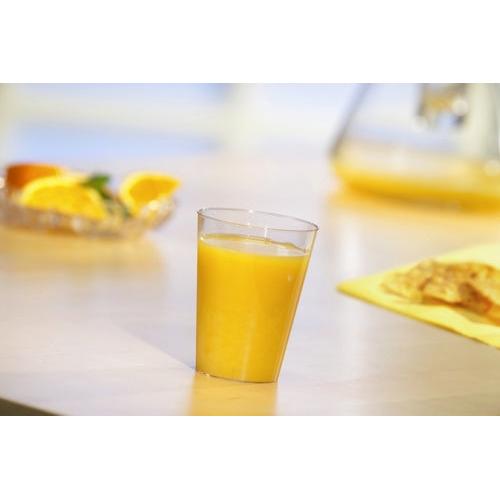 Ett Starpak 40 dricksglas, PS 0,1 l Ø 5,5 cm · 7,5 cm kristallklart engångsglas är fyllt med apelsinjuice på ett ljust bord. I bakgrunden finns apelsinskivor och en kanna - idealisk för fester och evenemang.
