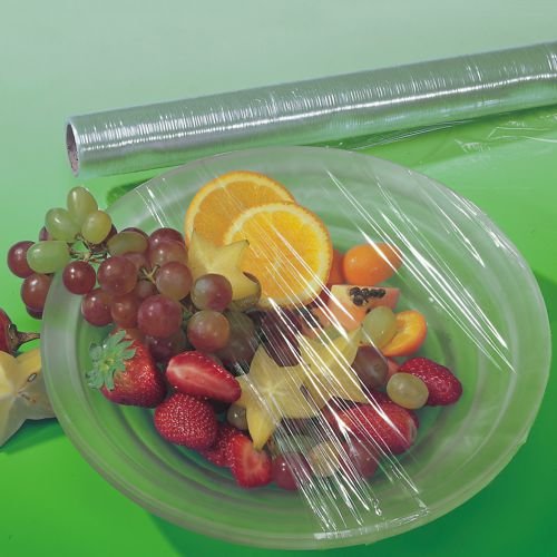 Ett genomskinligt blad Starpak plastfolie (30 m x 29 cm) täcker en tallrik med blandad frukt. I bakgrunden syns på en grön yta den rivstarka Starpak-plastfolierullen i sin vikbox (1 styck).