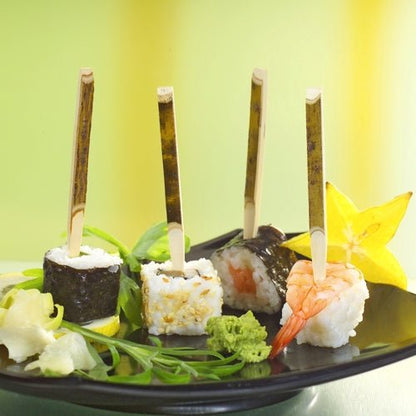 På en PAPSTAR pappbricka (200 stycken) ligger tre sushi-fingerfoods på PAPSTAR fingerfood-spett (11 cm naturträ), åtföljda av stjärnfrukt, wasabi, ingefära och grönt - perfekt för fester.