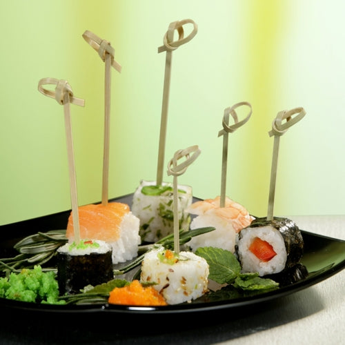 Präsentiert wird ein schwarzer Teller mit verschiedenen Sushi-Sorten, die jeweils mit einem PAPSTAR 250 Fingerfood-Picker „pure“ der PAPSTAR GmbH aufgespießt wurden. Garniert wird das Ganze mit Rogen, Blattgemüse und Wasabi; der Hintergrund ist in sanften Grün- und Gelbtönen gehalten.