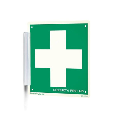 En grön-vit "Clip signera | Förpackning (1 styck)" från Orkla Wound Care AB med ett stort vitt kors och texten "Cederroth First Aid" fästs som en signaturstämpel med ett metallfäste på väggen och är väl synlig på arbetsplatsen.