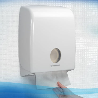 Eine Hand zieht ein Scott® ESSENTIAL™ Handtuch von Kimberly-Clark GmbH aus einem weißen, an der Wand montierten Spender in einer gefliesten Toilette; 15 Packungen à 340 Blatt pro Karton.