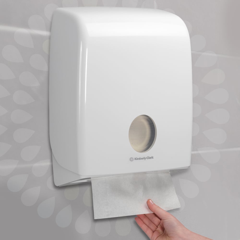 En hand drar ut en pappershandduk från en vit, väggmonterad dispenser som säkerställer hygienisk handtorkning. Idealisk för Kleenex® Ultra™ vikta handdukar - Interfold / vit (15 clips x 96 ark), från Kimberly-Clark GmbH.