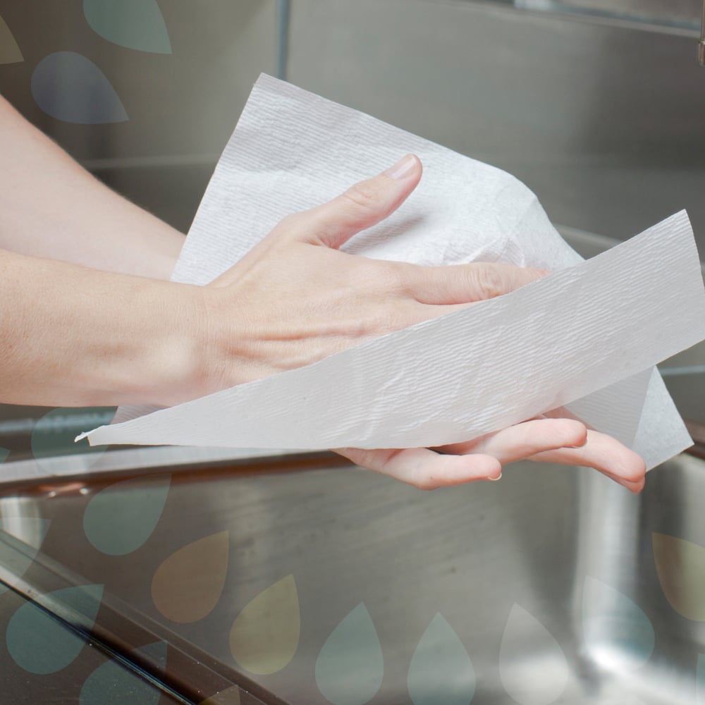 En person torkar sina händer med Kleenex® Ultra™ handdukar (Interfold, Vit, Stor, 30 x 94 ark) från Kimberly-Clark GmbH över en diskbänk i rostfritt stål.