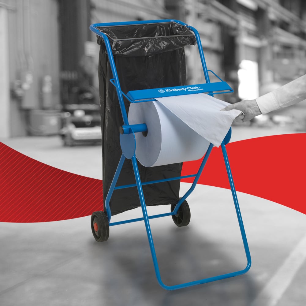 En person drar ut en WypAll® L20 pappershandduk för underhållsarbete - Stor rulle / Blå från Kimberly-Clark GmbH från en blå dispenser i en industriell miljö, med Kawasaki Robotics-logotypen och en svart sopsäck i närheten.