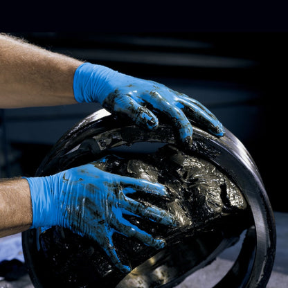 Mit KleenGuard® G10 2PRO Blaue Nitril-Handschuhe (23cm, beidhändig) von Kimberly-Clark GmbH trägt eine Person in einer industriellen Umgebung dickes schwarzes Fett auf ein großes Metalllager auf oder prüft es.