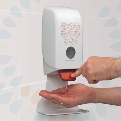 En person trycker på en röd spak på en väggmonterad Kleenex® Extra Gel Handdesinfektionsdispenser (Kimberly-Clark GmbH) och dispenserar klart handdesinfektionsmedel på deras hand. På framsidan finns en illustrerad instruktion, bakom finns mönstrade kakelplattor.