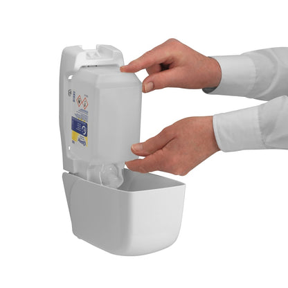 En person fyller på en väggmonterad dispenser av Kimberly-Clark GmbH Kleenex® Extra Gel Handdesinfektion genom att med båda händerna sätta in en ny genomskinlig 1-liters kassett; genom den öppna framsidan är endast deras händer och underarmar synliga.
