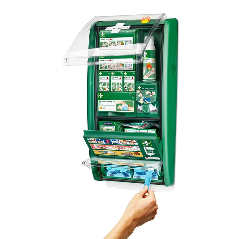 En väggmonterad Cederroth första hjälpen & brännskadestation från Orkla Wound Care AB är öppen och visar förbrukningsmaterial som förband, instruktioner, ögonsköljflaskor och en hand som tar en blå ögonsköljkapsel ur det nedre facket. (1 paket/kartong).