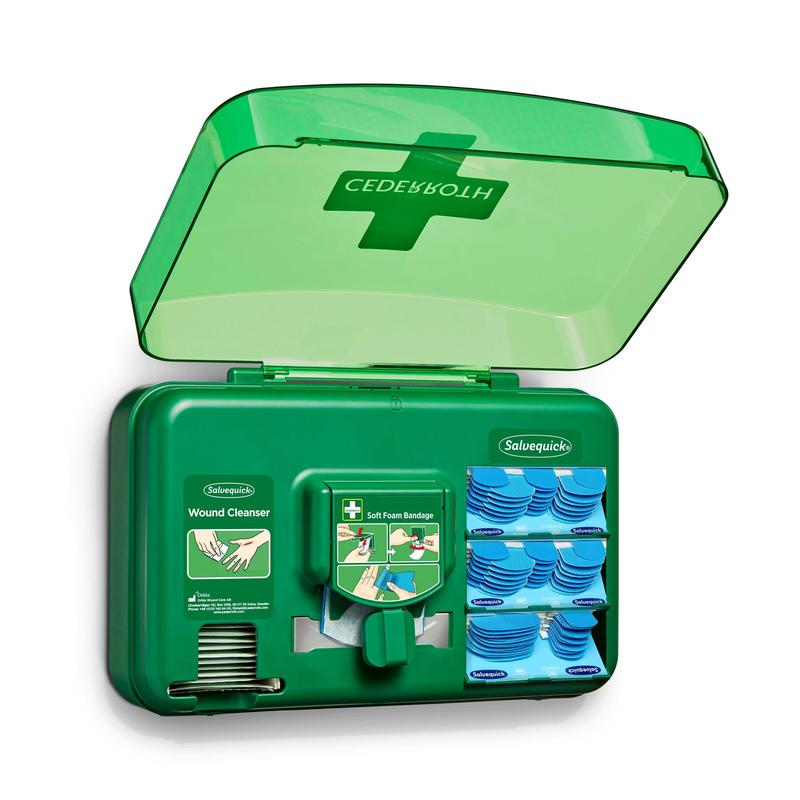 Ein blauer Wundversorgungsspender von Orkla Wound Care AB ist geöffnet und gibt den Blick frei auf Wundreinigungspakete, Pflaster und eine Rolle weicher Schaumstoffbinden, die in einzelnen Fächern angeordnet sind.