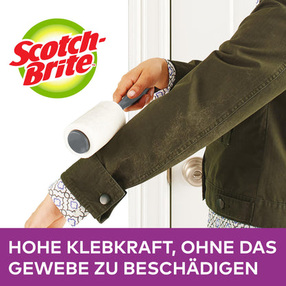 En person använder en Scotch-Brite™ Pet Extra Sticky* reservrulle för djurhår (48 blad, 1/förpackning) från 3M Deutschland GmbH på en mörkgrön jackärm. Text: "Hög klisterkraft, utan att skada tyget."
