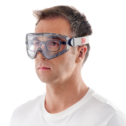 Ein Mann mit kurzen braunen Haaren und einem schlichten weißen T-Shirt trägt vor einem weißen Hintergrund die 3M™ Schutzbrille 2890, versiegelt, Klarsichtscheibe der 3M Deutschland GmbH mit einem weißen Gummiband mit der Aufschrift "3M.