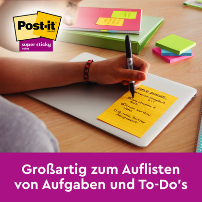 Jemand schreibt eine To-Do-Liste auf einem gelben Post-it® Super Sticky Note (Großformat, Verschiedene Farben, 45 Blatt/Block, 100% PEFC) der 3M Deutschland GmbH auf einem Laptop. Weitere bunte Haftnotizen und Notizbücher sind auf dem Schreibtisch zu sehen.