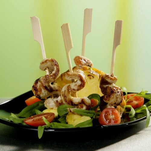 PAPSTAR Grillspett 21 cm ”Golf” från PAPSTAR GmbH: Perfekta grillspett med kyckling och ananas på färska sallader med körsbärstomater, serverade på en svart tallrik mot en grön-gul bakgrund. 250 stycken i en kartongbricka.