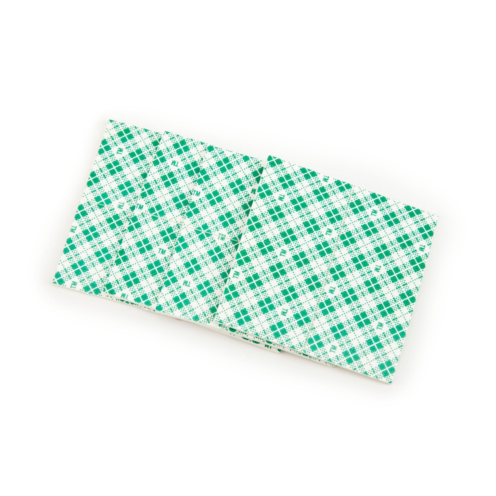 Zwei Scotch-FIX™ Doppelseitige Innenmontagequadrate (25mm x 25mm) von 3M Deutschland GmbH liegen nebeneinander und zeigen ihre grün und weiß gemusterte Rückseite.