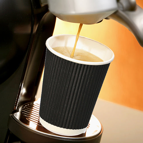 En Starpak 25 drickbägare, pappers "To Go" Ripple Wall-bägare står på en metalldroppbricka under utloppsröret på en kaffemaskin medan het kaffe rinner in, och framhävs mot en mjukt belyst, varmt tonad bakgrund.