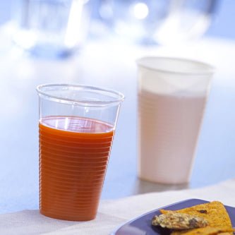 En Starpak 25 drickbägare, PP 0,2 l (Ø 7,03 cm · 9,9 cm), fylld med apelsinjuice, står i förgrunden bredvid en vit kopp med ljus dryck; nedre högra hörnet visar en blå tallrik med mat – idealisk för resan.