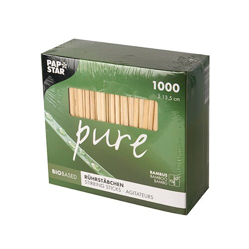 En grön låda med texten 'pure' innehåller 1000 PAPSTAR bambus omrörningspinnar (13,5 cm, biologiskt nedbrytbara). Uppe till vänster finns logotypen för PAPSTAR GmbH; ikoner visar det miljövänliga bambusmaterialet i förpackningen.
