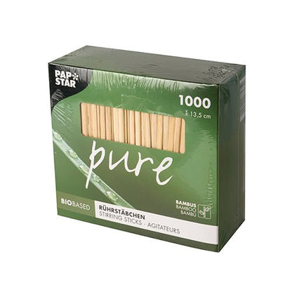 En grön låda med texten 'pure' innehåller 1000 PAPSTAR bambus omrörningspinnar (13,5 cm, biologiskt nedbrytbara). Uppe till vänster finns logotypen för PAPSTAR GmbH; ikoner visar det miljövänliga bambusmaterialet i förpackningen.