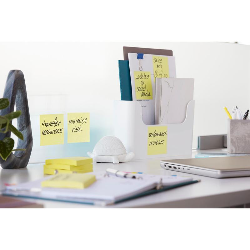 På ett vitt skrivbord står en dokumenthållare med mappar, en sköldpaddsfigur, en krukväxt, en stängd laptop, kontorsmaterial och 3M Deutschland GmbH Post-it® Super Sticky Notes (Gul, 76x127mm), 90 blad/block, stark vidhäftningskraft.