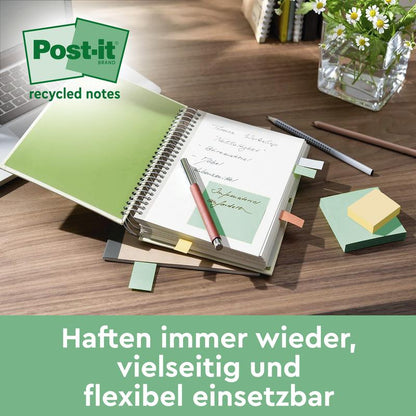 Ett skrivbord med en uppslagen anteckningsbok, där en grön Post-it® Super Sticky 100 % återvinningslapp (76x76 mm, 70 blad/block, 100% PEFC) från 3M Deutschland GmbH ligger, omgiven av klisterlappar, penna, pennhållare och glasvas. Text: "Fäster om och om igen."
