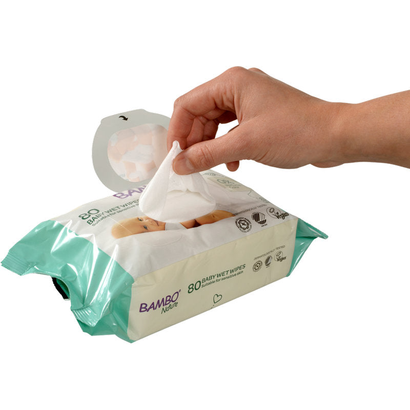 En hand drar ut en Bambo Nature våtservett med klisterförslutning (15x20cm, 80 stycken) från Abena Re-Seller GmbH ur sin ljusgrön-vita förpackning, som är designad med ikoner och text på framsidan för känslig babyhud.