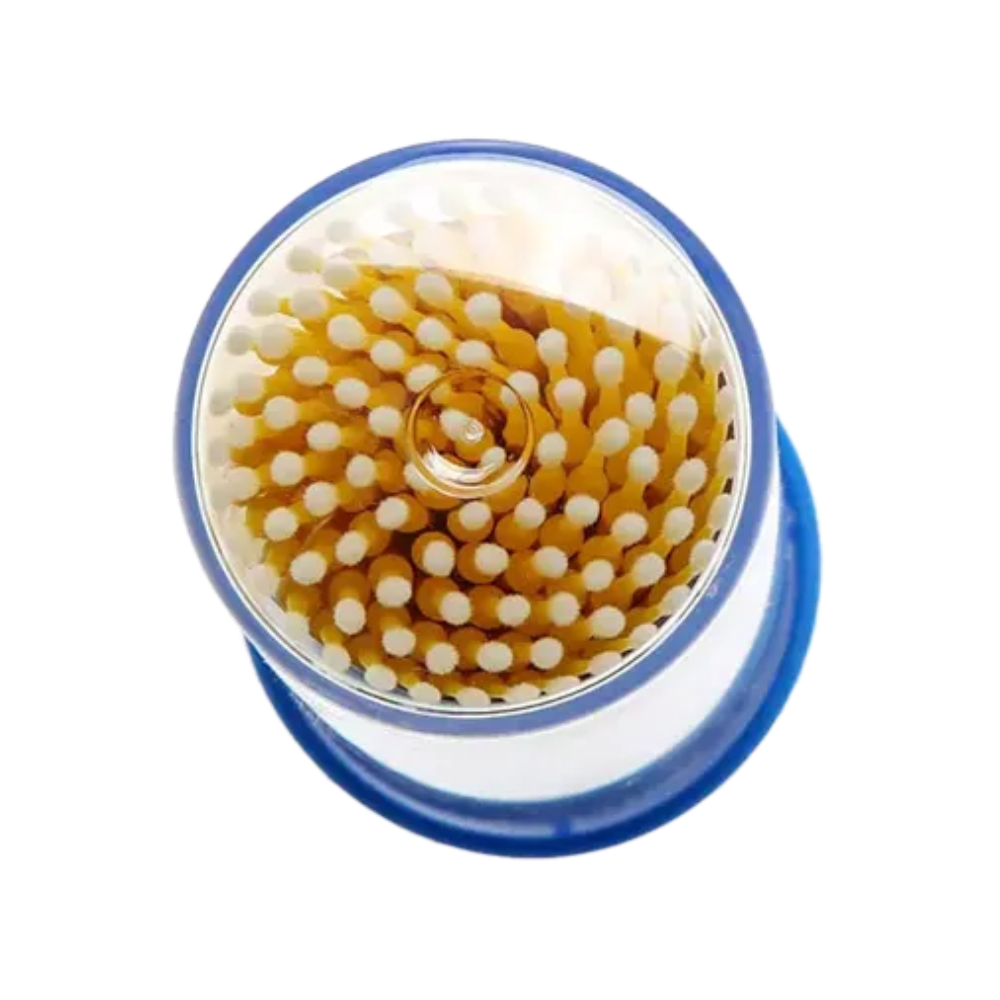 En vy ovanifrån visar AMPri MED-COMFORT engångsmikroapplikatorer, idealiska för exakt arbete. Dessa applikatorer är prydligt arrangerade i ett cirkulärt mönster, med vita spetsar och bruna stjälkar. Den genomskinliga behållaren har en blå botten eller lock, som påminner om grundläggande tandvårdsprodukter.