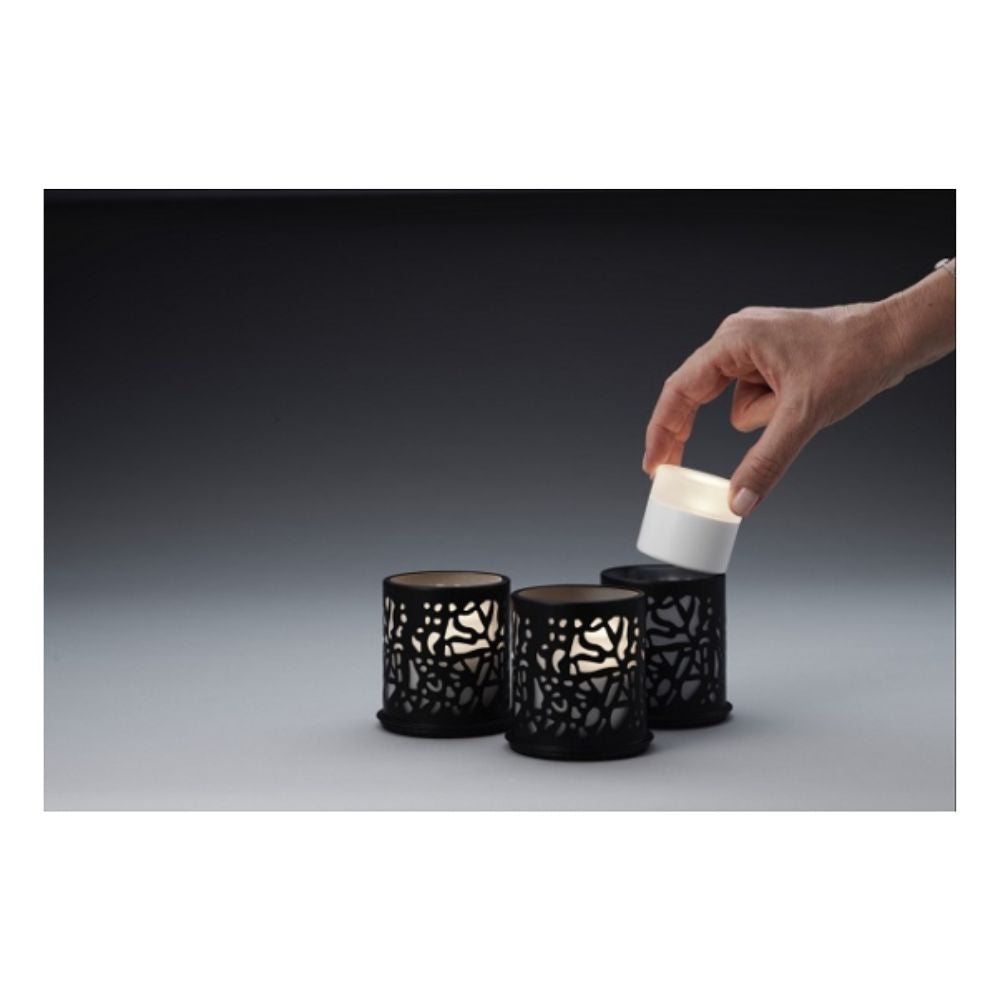 En hand lyfter ett litet vitt LED-ljus från en svart hållare, medan två identiska Duni GmbH Multicolour LED Set, Mini - 8 stycken i liknande hållare vilar på en grå yta mot en mörk bakgrund.