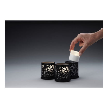 En hand lyfter ett litet vitt LED-ljus från en svart hållare, medan två identiska Duni GmbH Multicolour LED Set, Mini - 8 stycken i liknande hållare vilar på en grå yta mot en mörk bakgrund.