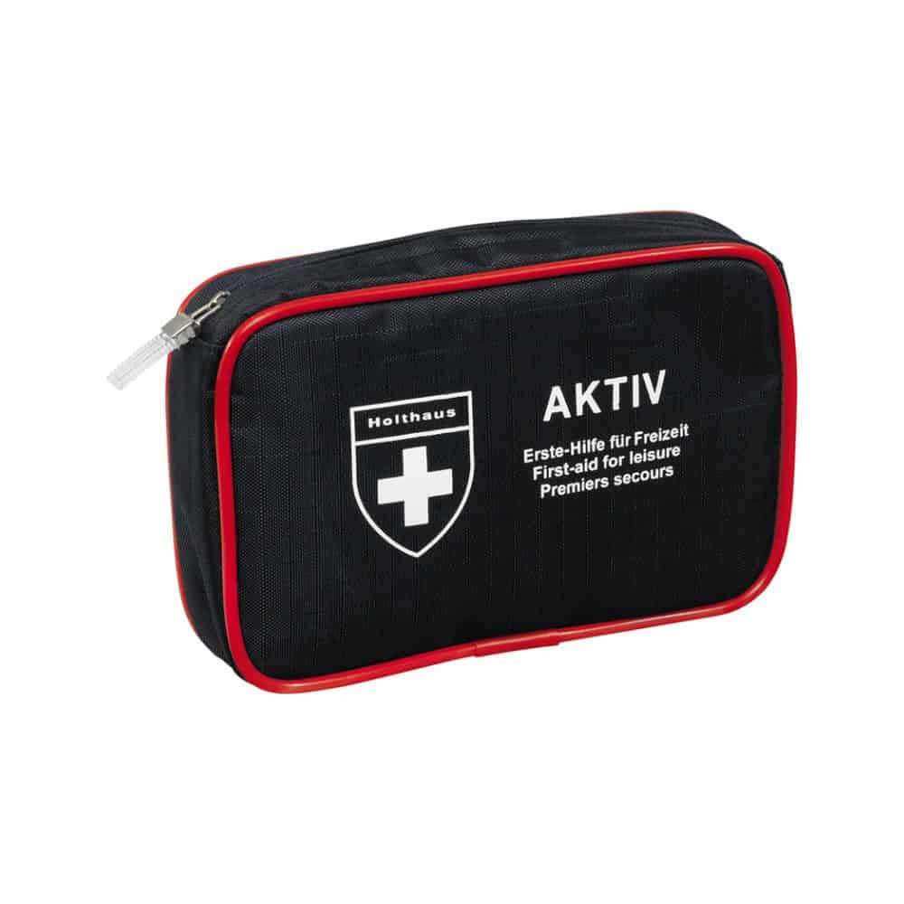 Ett kompakt svart första hjälpen-kit med röd kant och dragkedja, en vit korslogga och texterna ”Holthaus Medical AKTIV” och ”Första hjälpen för fritid / First-aid for Leisure / Premiers secours” på framsidan. Perfekt för resor och hemmet.