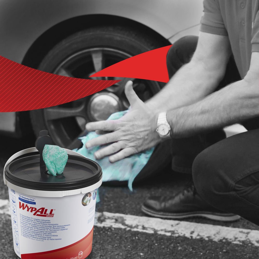 En person knäböjer för att rengöra bilhjul med gröna WypAll® torkdukar från Kimberly-Clark GmbH. I förgrunden finns en synlig behållare med 6 hinkar x 90 ark. Den svartvita bakgrunden har en stark röd grafisk accent.