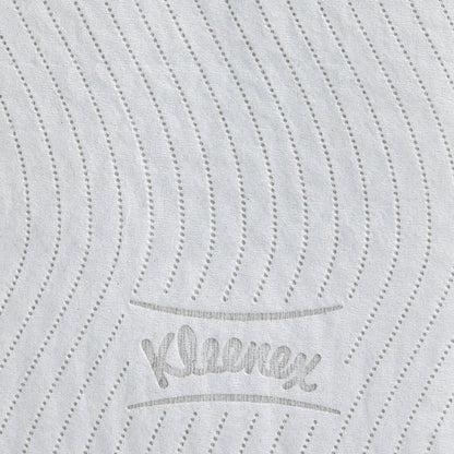 Närbilden av en vit Kleenex® toalettpappersrulle från Kimberly-Clark GmbH visar prickade, vågiga linjer och den i grått präglade texten "Kleenex", som framhäver den högkvalitativa texturen hos denna 8-pack (12 små rullar à 250 ark).
