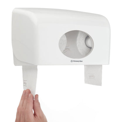 En hand drar Kimberly-Clark GmbH Kleenex® toalettpappersrullar (vit, 8 förpackningar x 12 små rullar, 250 ark vardera) från en dubbelväggsdispenser med ovalt fönster - idealisk för användning med denna kartong (8 förpackningar).