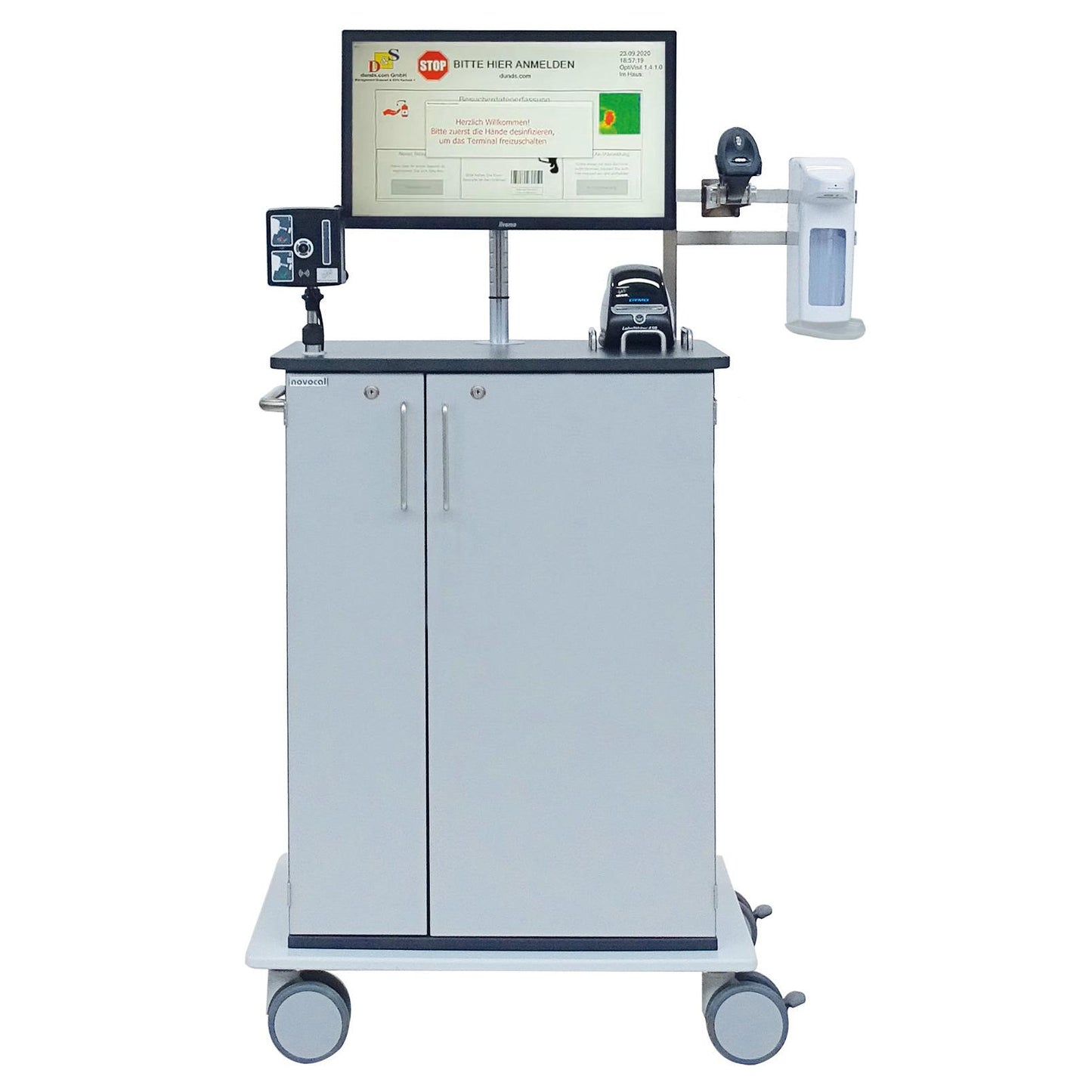 Novocal EDV-vagnen Typ Optivisit är en mobil medicinsk arbetsstation med bildskärm, streckkodsläsare, desinfektionsmedel och skrivare i ett grått tvådörrars skåp med fyra länkhjul. Märke: Novocal.