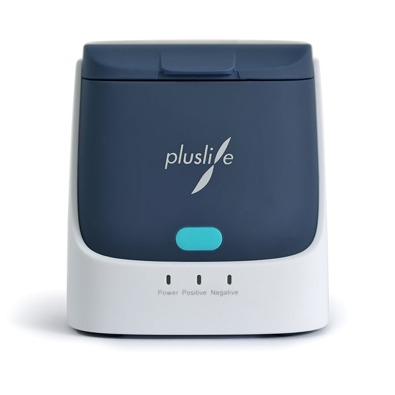 Pluslife Mini Dock PoC-NAT-testenheten är en kompakt, mörkgrå och vit elektronisk enhet med logotypen „pluslife“. Den ger laboratorieexakta testresultat för precisa Point-of-Care-tester med sin blå knapp och de tre kontrollamporna märkta „Power“, „Positiv“ och „Negativ“.