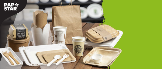 Nachhaltiges Einweggeschirr von PAPSTAR aus umweltfreundlichen Materialien, stilvoll arrangiert auf einem Holztisch. Abgebildet sind unter anderem Papiertragetaschen, Pappbecher mit „100 % paper“- und „PURE JOY“-Aufdruck, braune und weiße Take-away-Schalen, Holzbesteck, Kartonschalen sowie Palmblatt-Teller. Oben rechts ist das „Green Brand Germany 2024/2025“-Siegel zu sehen. Links befindet sich das PAPSTAR-Logo auf einem grünen und schwarzen Hintergrund.
