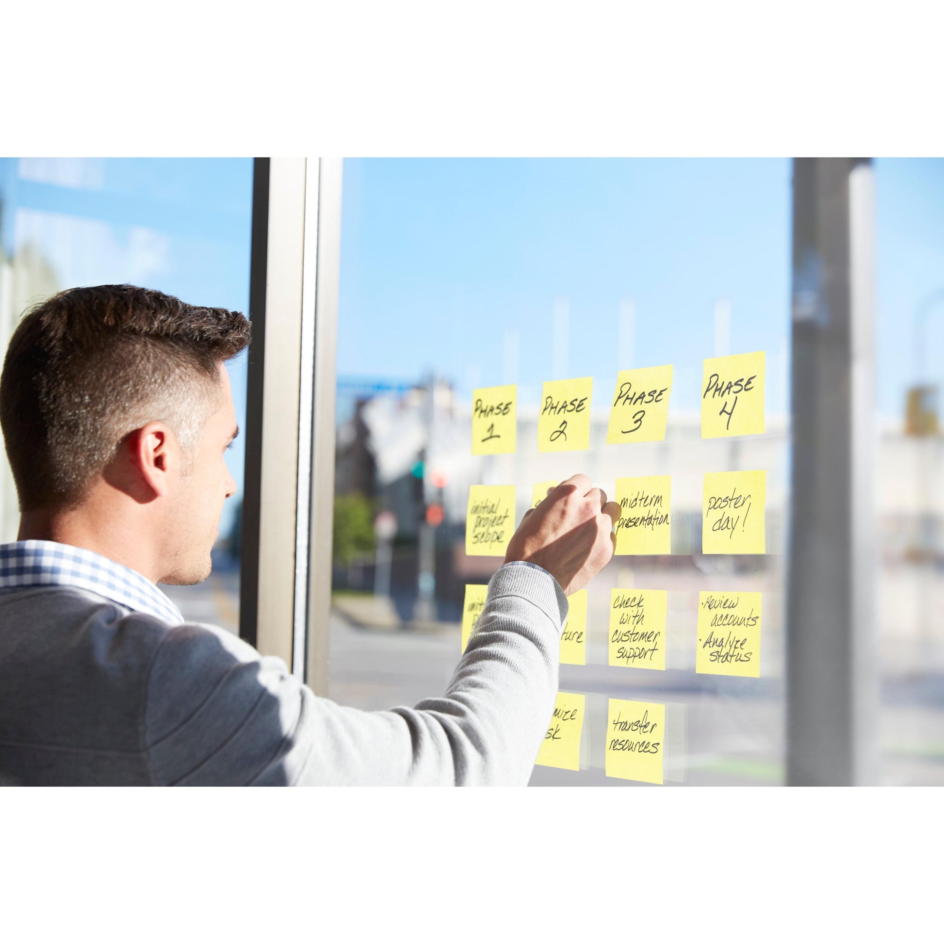 Ein Mann organisiert Projektphasen und Aufgaben auf einem Glasfenster mit Post-it® Super Sticky Notes, Gelb (51 mm x 76 mm), 3M Deutschland GmbH, während das Sonnenlicht über eine städtische Straße fällt. Jede Packung enthält 12 Blöcke à 90 Blatt in einer PEFC-zertifizierten Kartonverpackung.